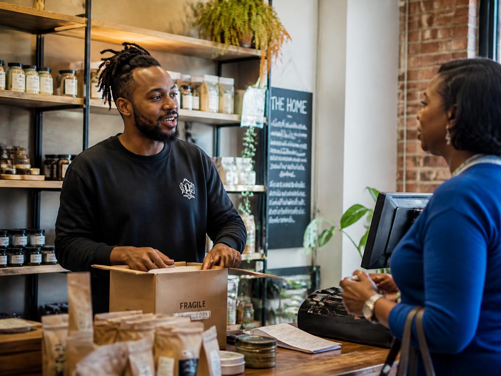 A Black entrepreneur talking with a customer while working behind the counter of a small business